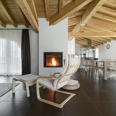 armcahir near to fireplace in the living room of a apartment overlooking on the dining room with wood ceiling